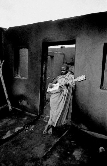 3.Ragazzo suona la chitarra fatta con lattine dolio tra le rovine bruciate della sua casa dura