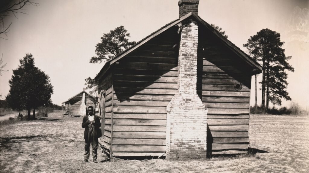 15. Walker Evans – Il fotografo dallo sguardo discreto tra realtà e poesia 26 26.Man Posing for Picture in front of Wooden House 1936 by Walker Evans