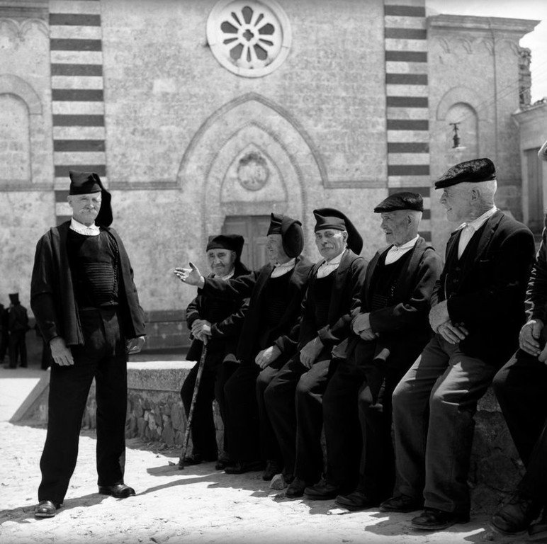 27. Un gruppo di uomini in abito tradizionale sintonizzati su un muretto in Piazza Parrocchia a Osilo Provincia di SassariSardegna 1956. Jean Dieuzaide